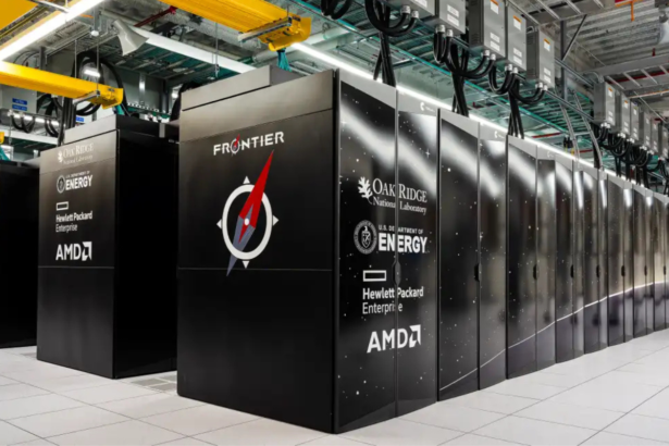 Rows of black server cabinets labeled "FRONTIER" in a data center with yellow overhead cranes at Oak Ridge National Laboratory.